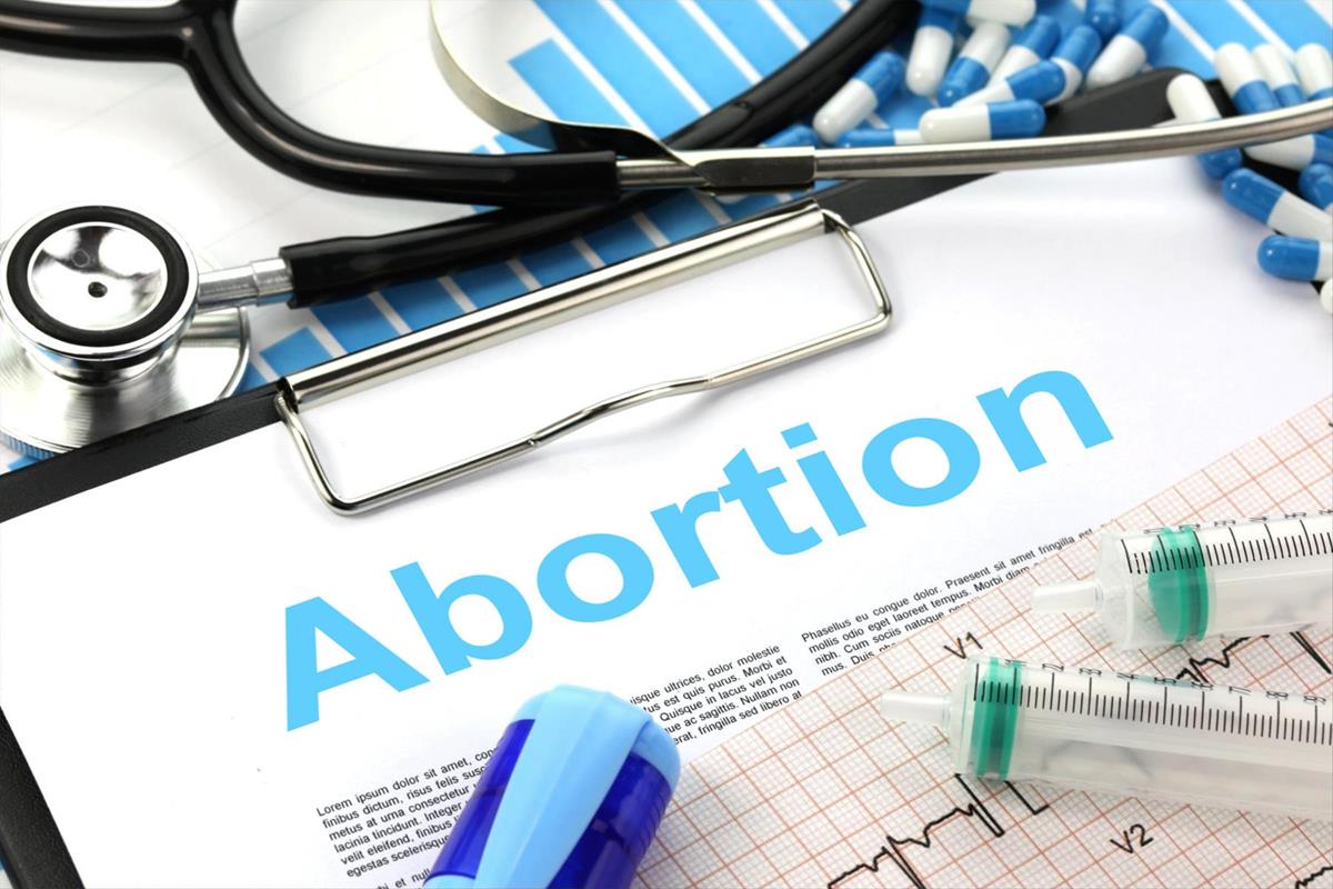 A clipboard with blue text that says 'Abortion,' surrounded by blue and white pills